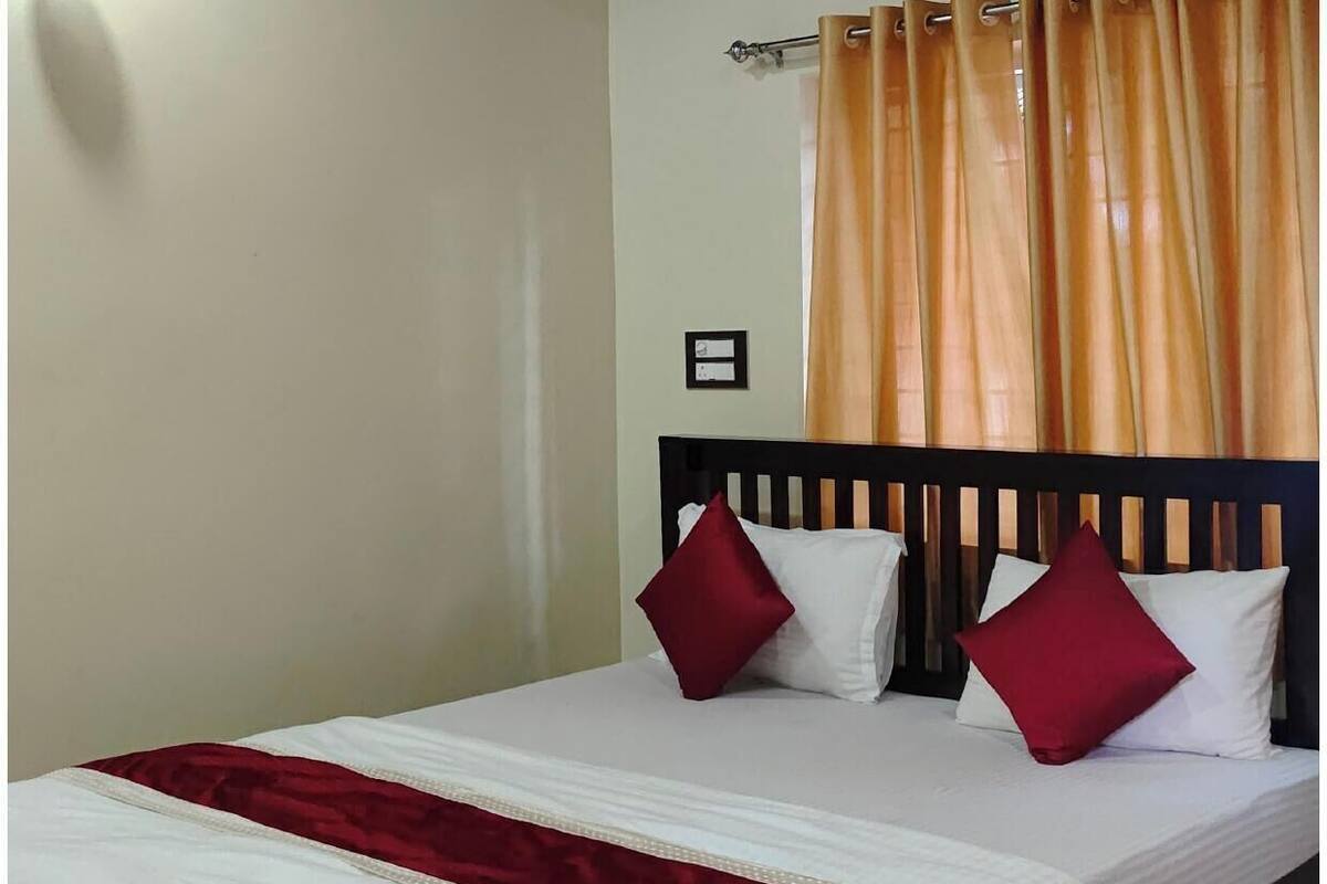 Una cama bien tendida con una colcha blanca y roja, dos almohadas rojas y un cabecero de madera.
