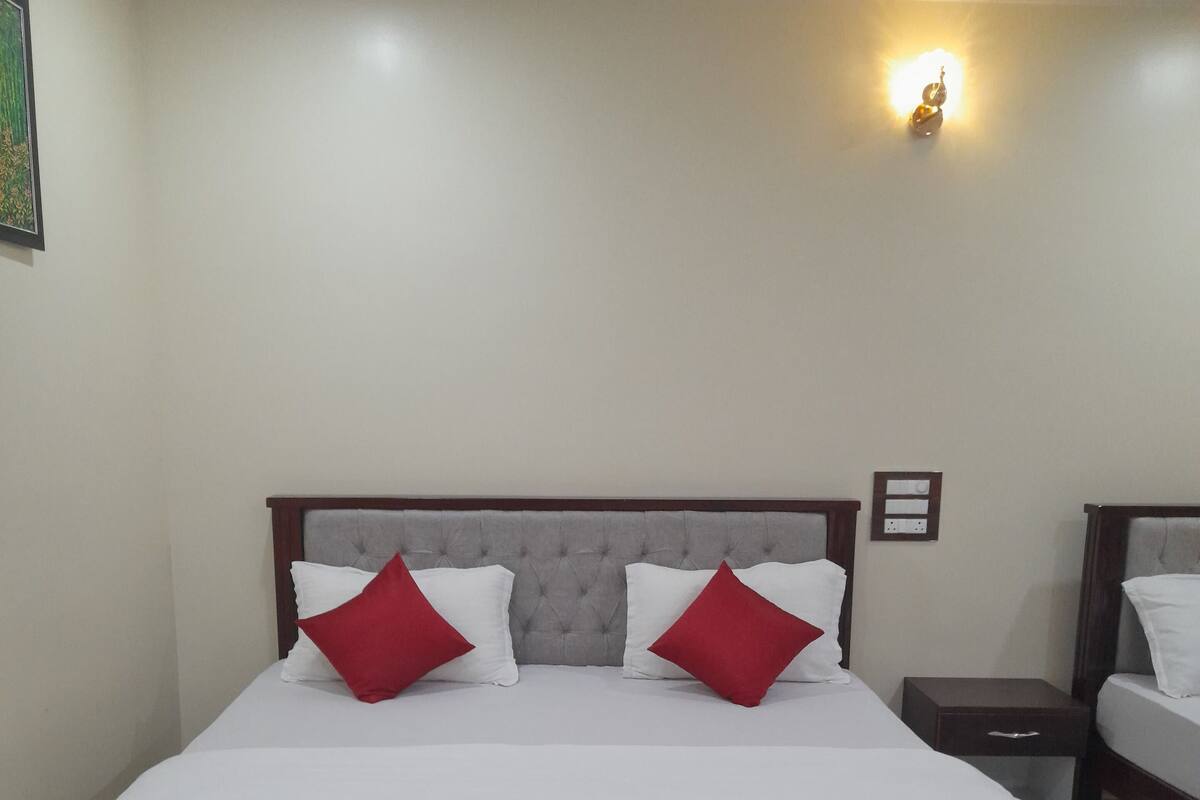Una cama bien hecha con estructura de madera, dos almohadas rojas y una colcha blanca.