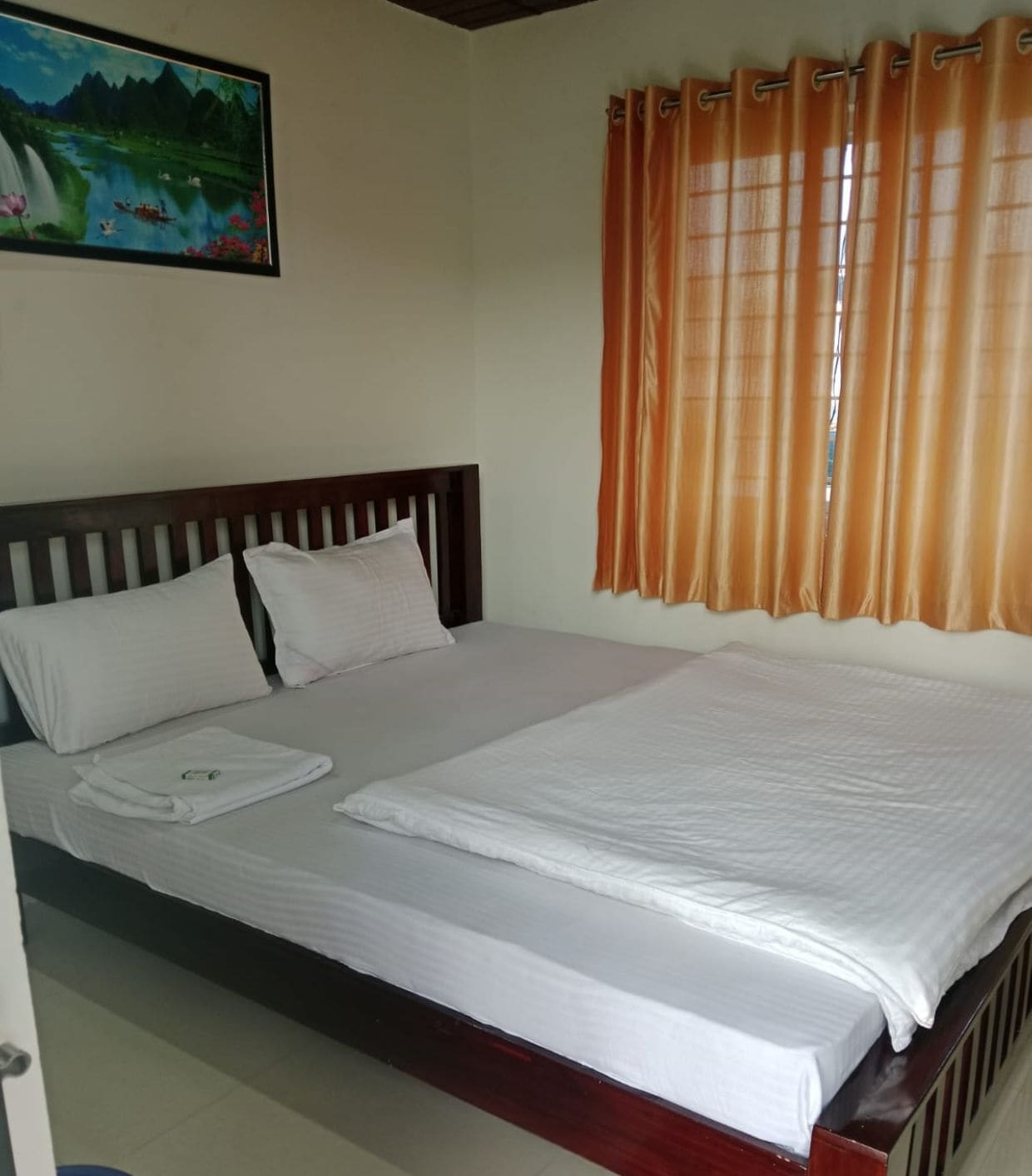 A double room with a wooden bed, white bedding, and orange curtains.