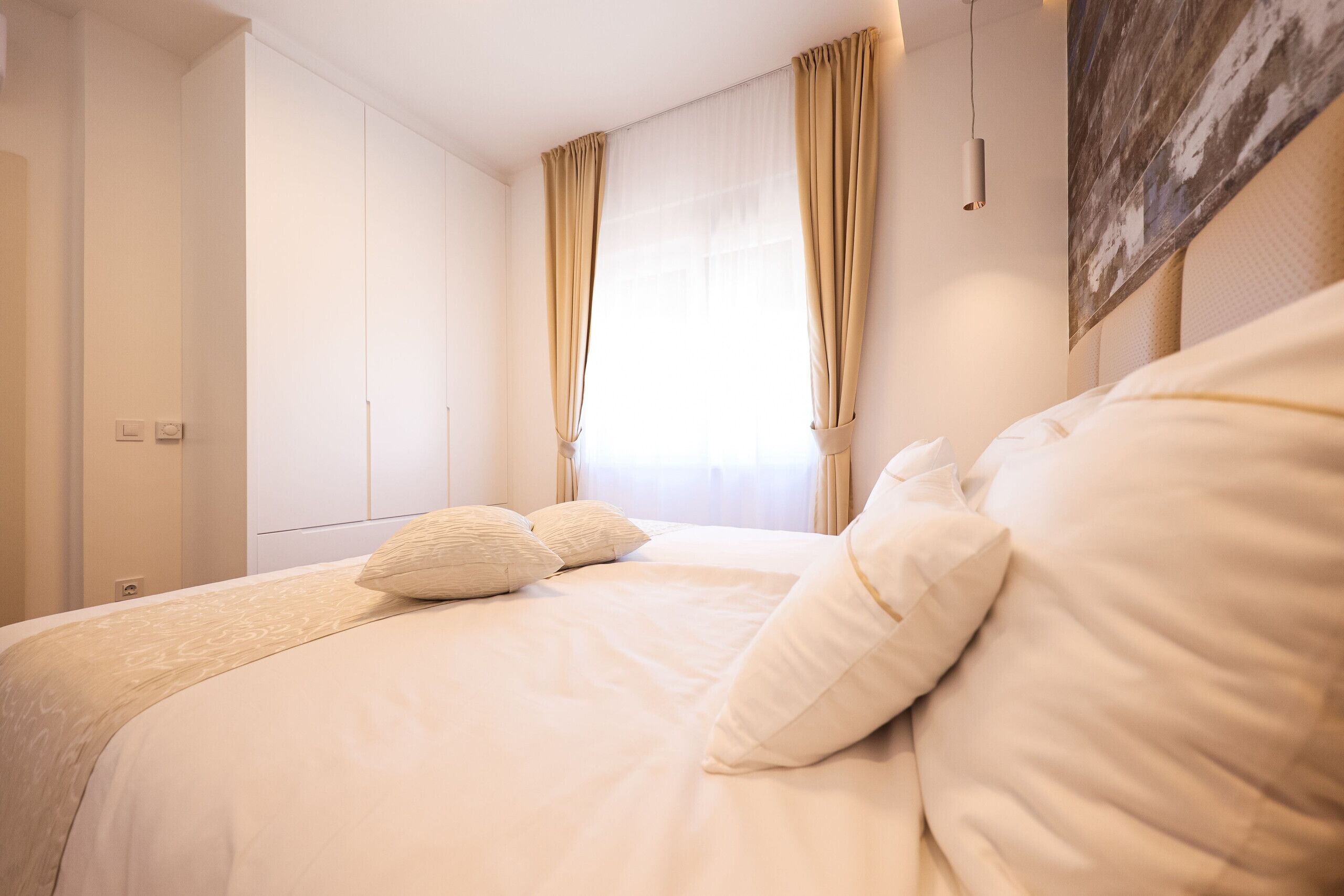 A bedroom with a large bed, beige curtains, and a wall-mounted light fixture.