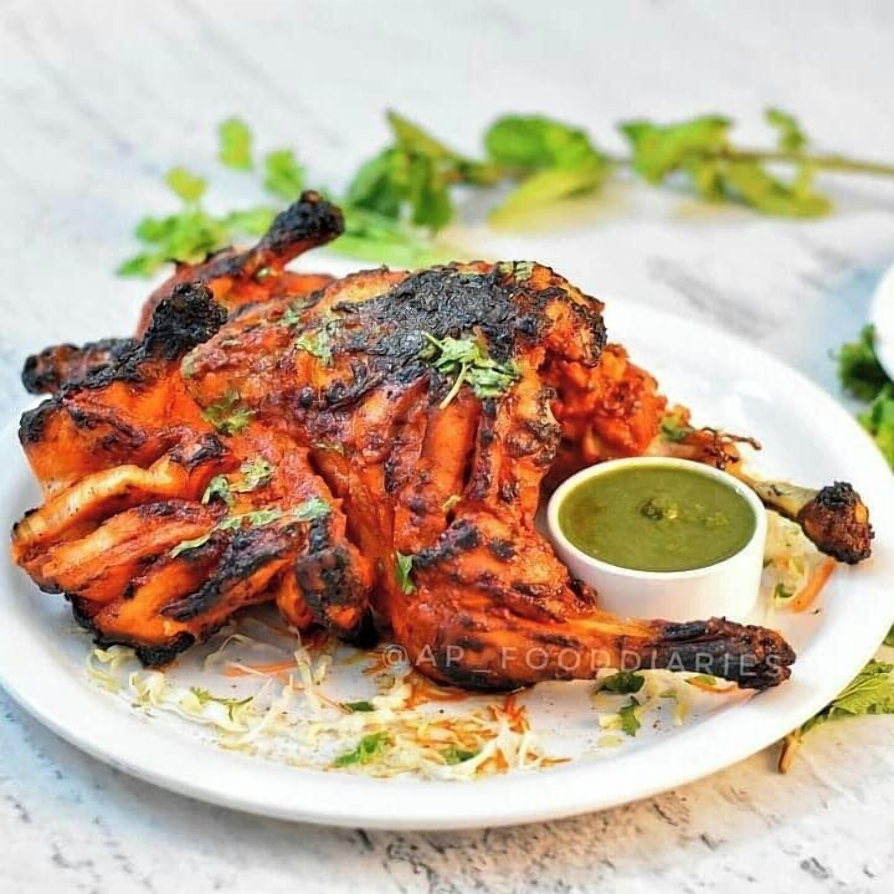 Ein Teller mit Tandoori-Hähnchen, dazu grüner Chutney und Krautsalat.