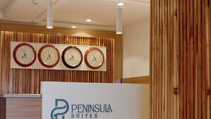 Een receptiebalie met een bord voor Peninsula Suites, houten lambrisering en vier klokken aan de muur.