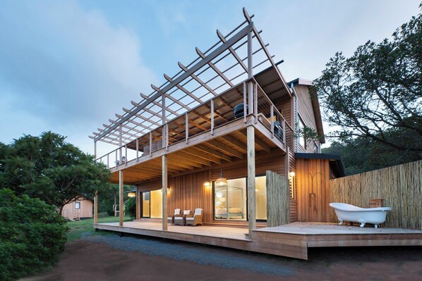 A modern house with a wooden deck, a covered outdoor seating area, and a visible bathtub.
