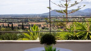 A balcony with a view of a rural landscape, including fields and distant mountains.