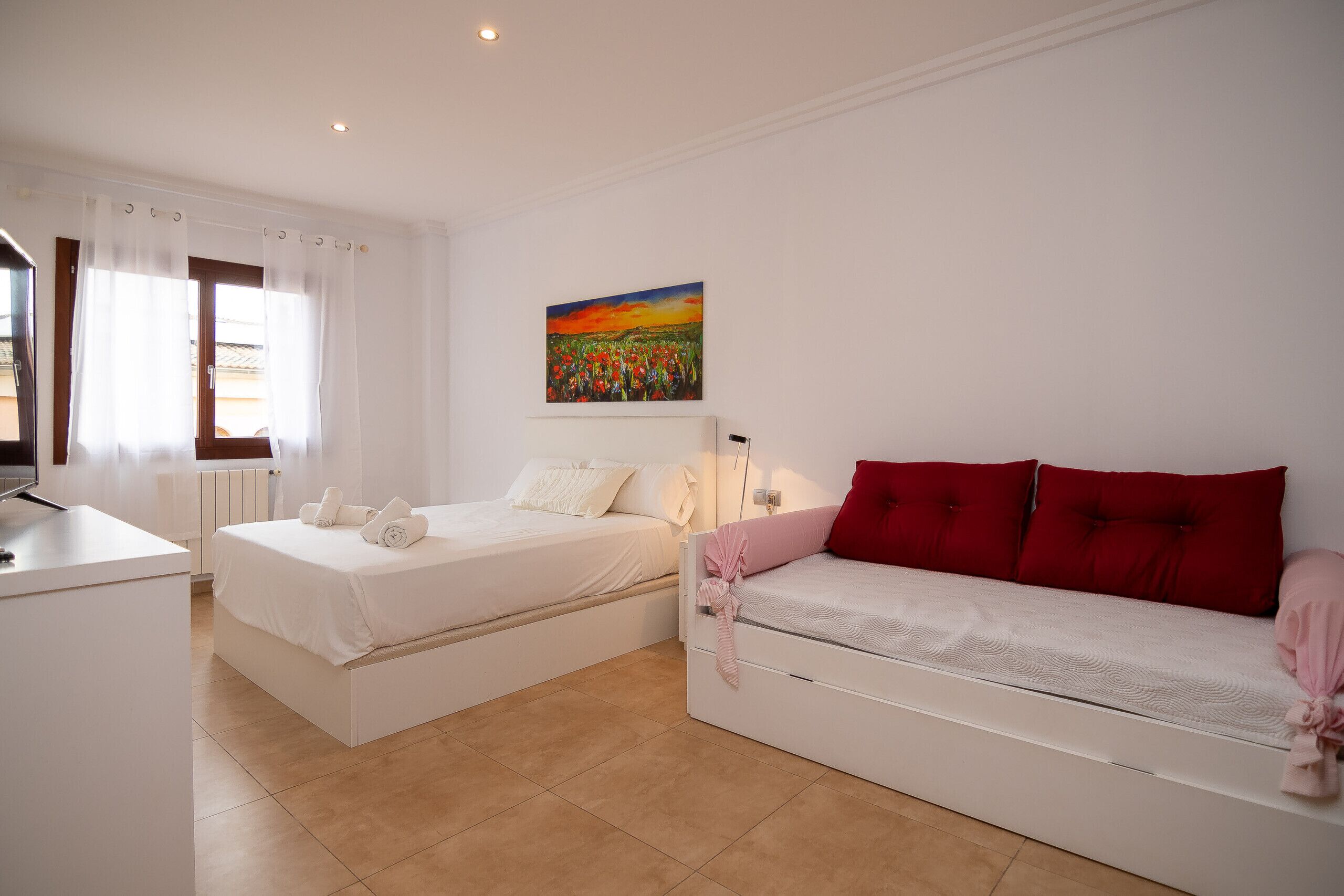 A bedroom with two beds, a desk, and a painting on the wall.