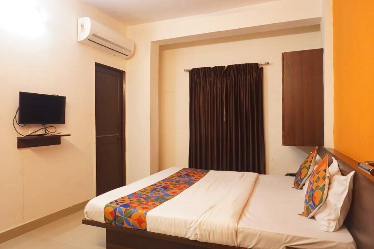 A hotel room with a bed, a television on a shelf, an air conditioning unit, a door, and a curtain.