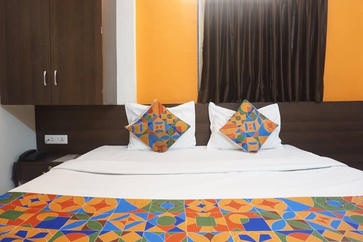 A hotel room with a bed, two pillows with geometric patterns, a nightstand, and a wall with a curtain.