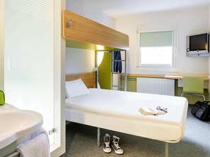 Una habitación de hotel compacta con una litera, un escritorio pequeño, un televisor y una ventana.