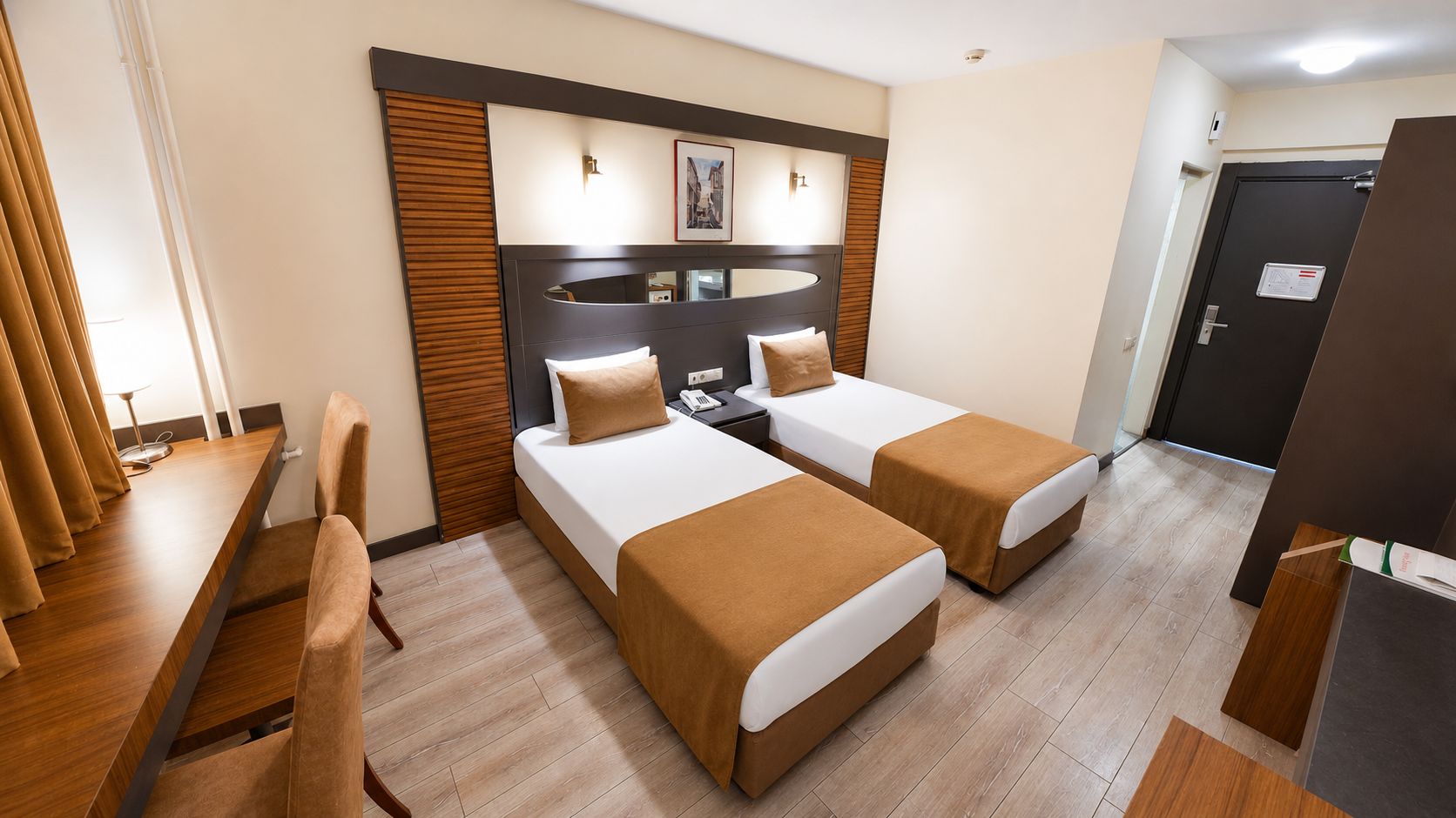A hotel room with two beds, a desk, a chair, and a wooden floor.