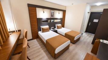 A hotel room with two beds, a desk, a chair, and a wooden floor.