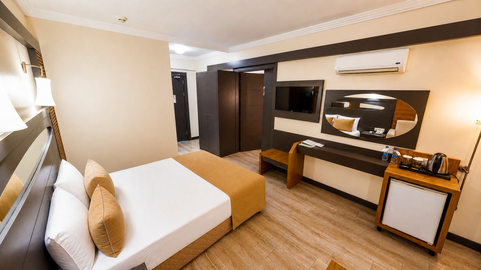 Una habitación de hotel con cama, mesita de noche, escritorio, silla y una pequeña cocina.