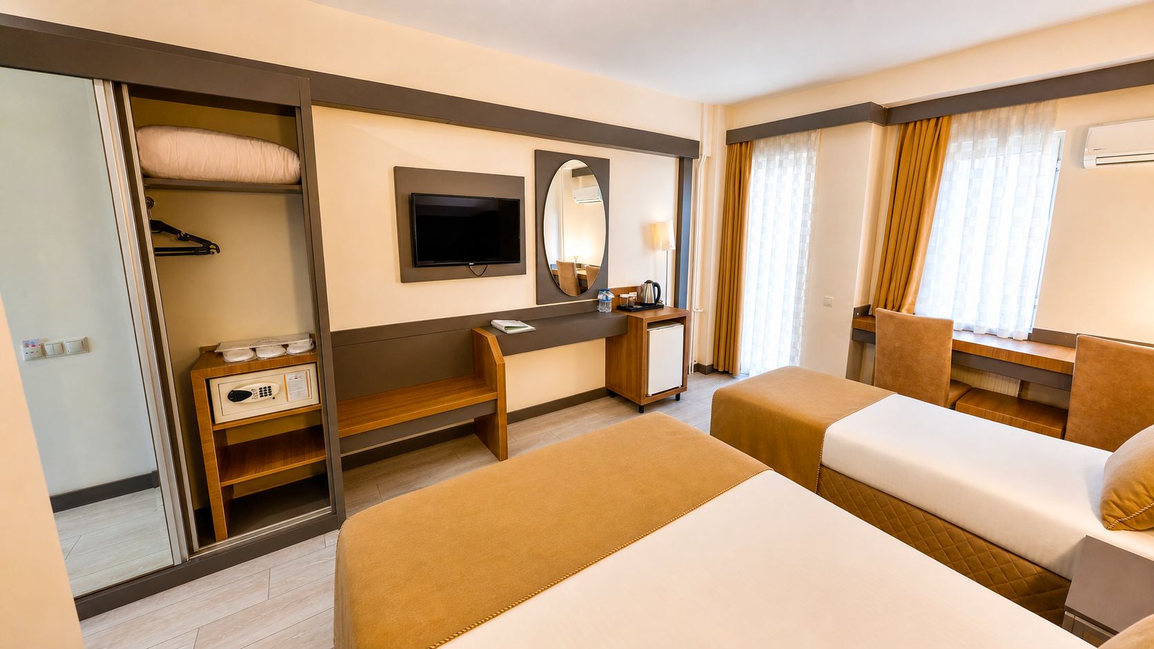 Una habitación de hotel con dos camas, un escritorio, un espejo, un televisor y un armario.