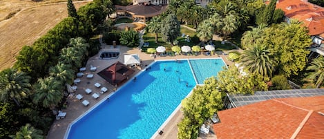 An aerial view of a resort with a large swimming pool surrounded by palm trees and lounge chairs.