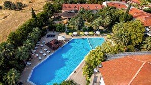 Luchtbeeld van een resort met een groot zwembad, omringd door palmbomen en ligbedden.