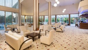 A spacious lobby with white leather sofas, a coffee table, and a reception desk. Large windows provide natural light and views of greenery outside. - Lycus River Thermal Hotel (Denizli)