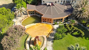 An aerial view of a large, modern building with a curved roof and a swimming pool. - Lycus River Thermal Hotel (Denizli)