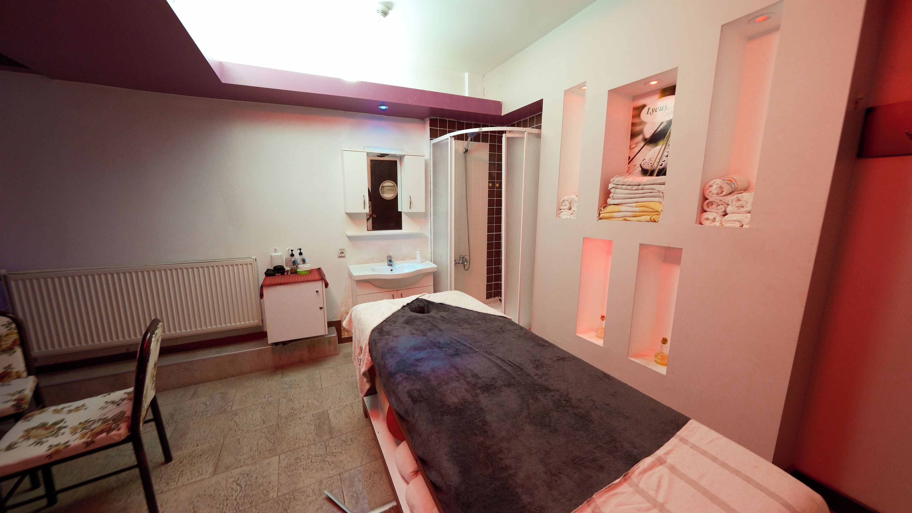 A room with a bed, a chair, a sink, and a shower.
