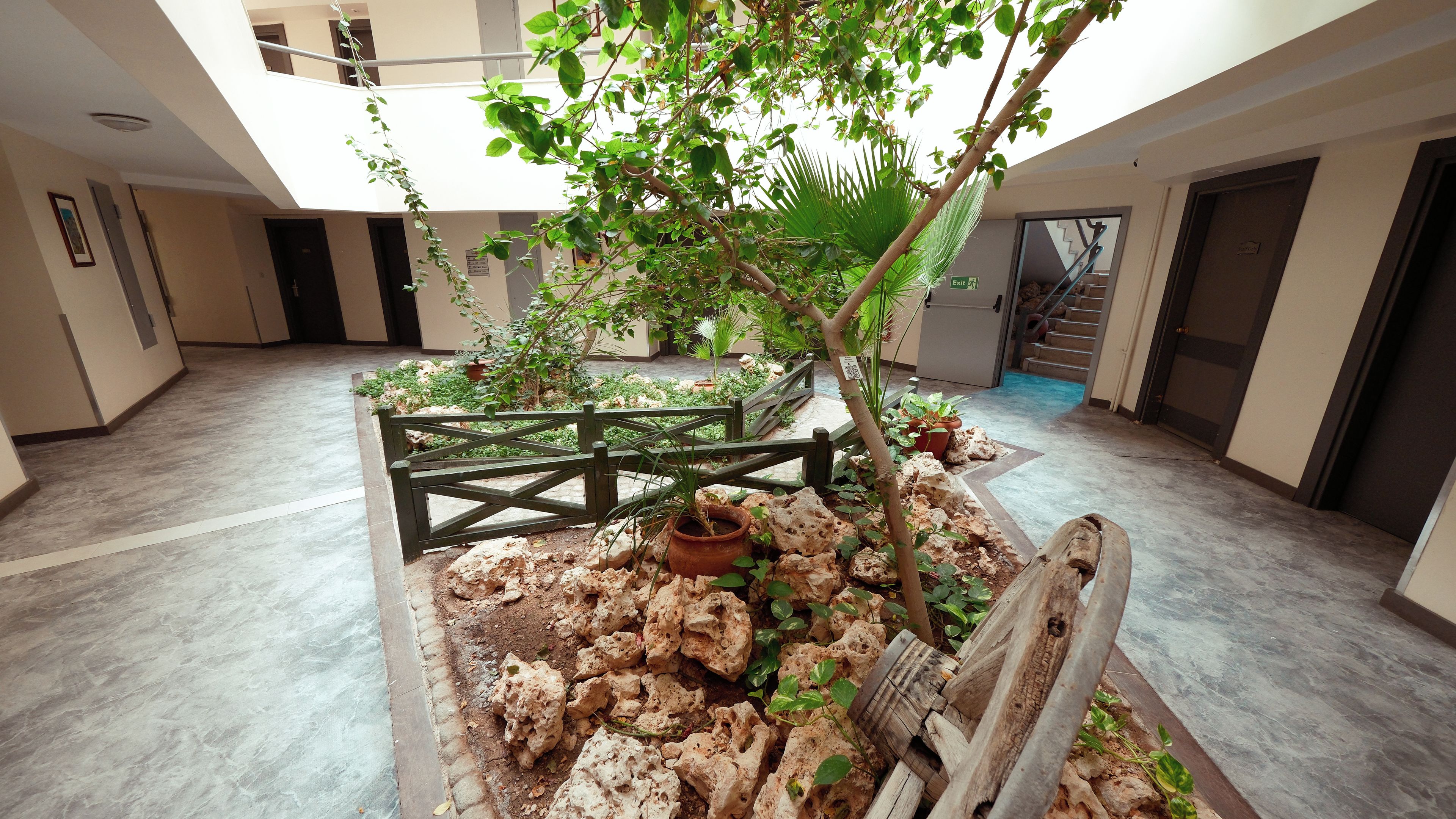 A spacious indoor atrium with a central garden area featuring a wooden fence, potted plants, and a small tree.