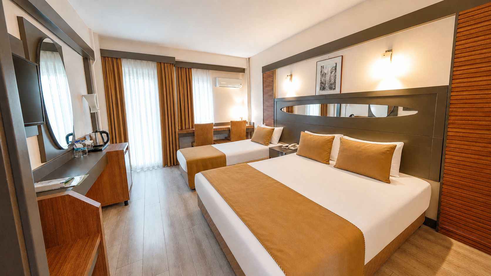 A hotel room with two beds, a desk, a mirror, and a wall-mounted light fixture.