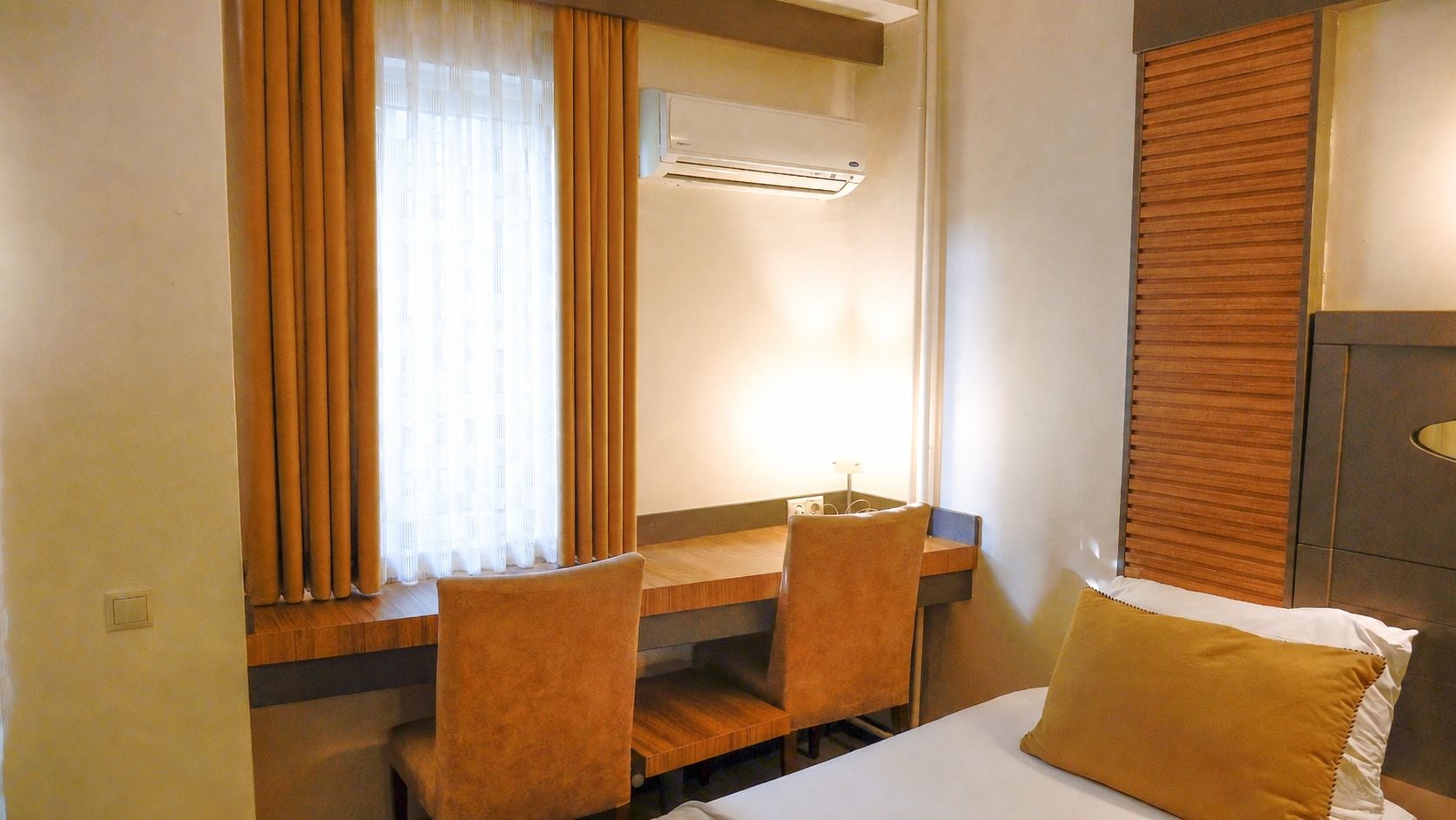 Une chambre d’hôtel comprenant un lit, un bureau avec deux chaises, une fenêtre avec des rideaux et un appareil de climatisation.