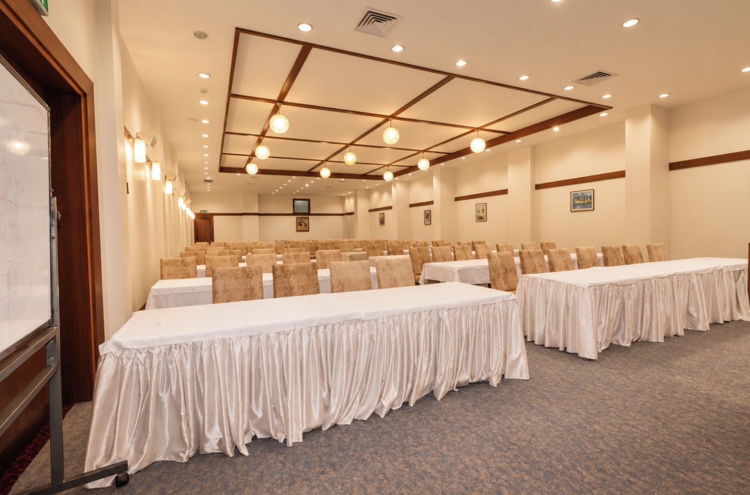 A conference room with rows of tables and chairs, a whiteboard, and ceiling lights.