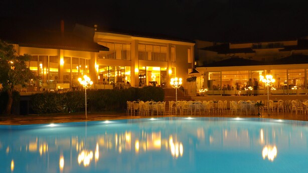 Un hotel con piscina, mobiliario exterior y fachada bien iluminada.