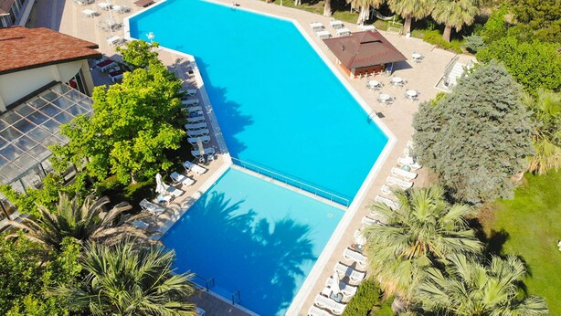 An aerial view of a hotel with a large swimming pool, surrounded by palm trees and lounge chairs. - Lycus River Thermal Hotel (Denizli)