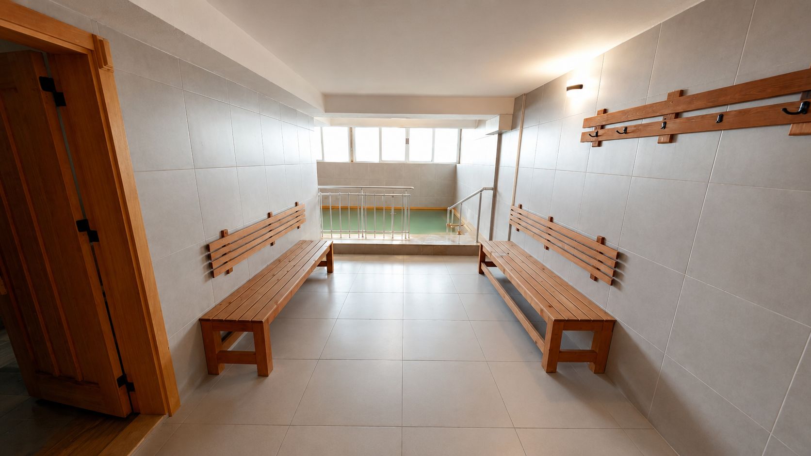 Una habitación con dos bancos de madera, un vidrio y vista a una piscina a través de una ventana.