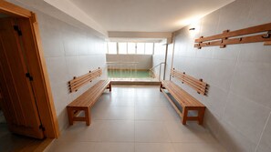 Una habitación con dos bancos de madera, un vidrio y vista a una piscina a través de una ventana.
