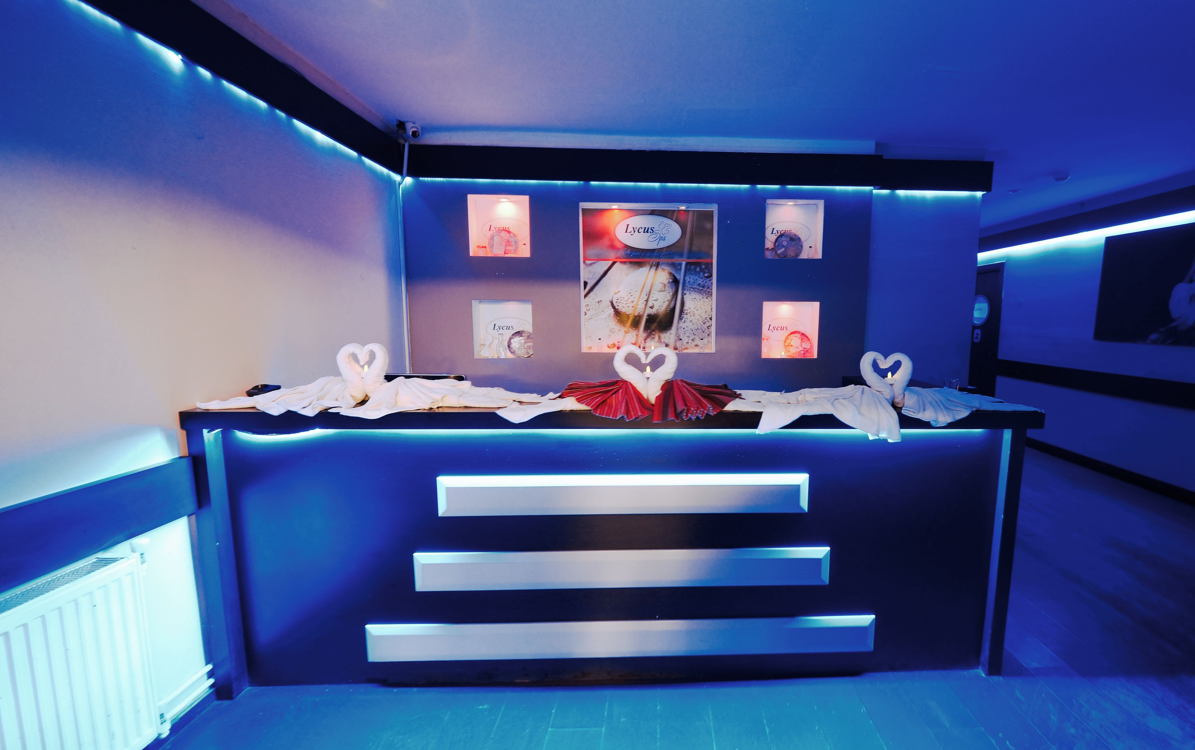 Un mostrador de recepción con una disposición de toallas con forma de corazón, una obra de arte enmarcada encima y una escalera que conduce a un nivel superior.