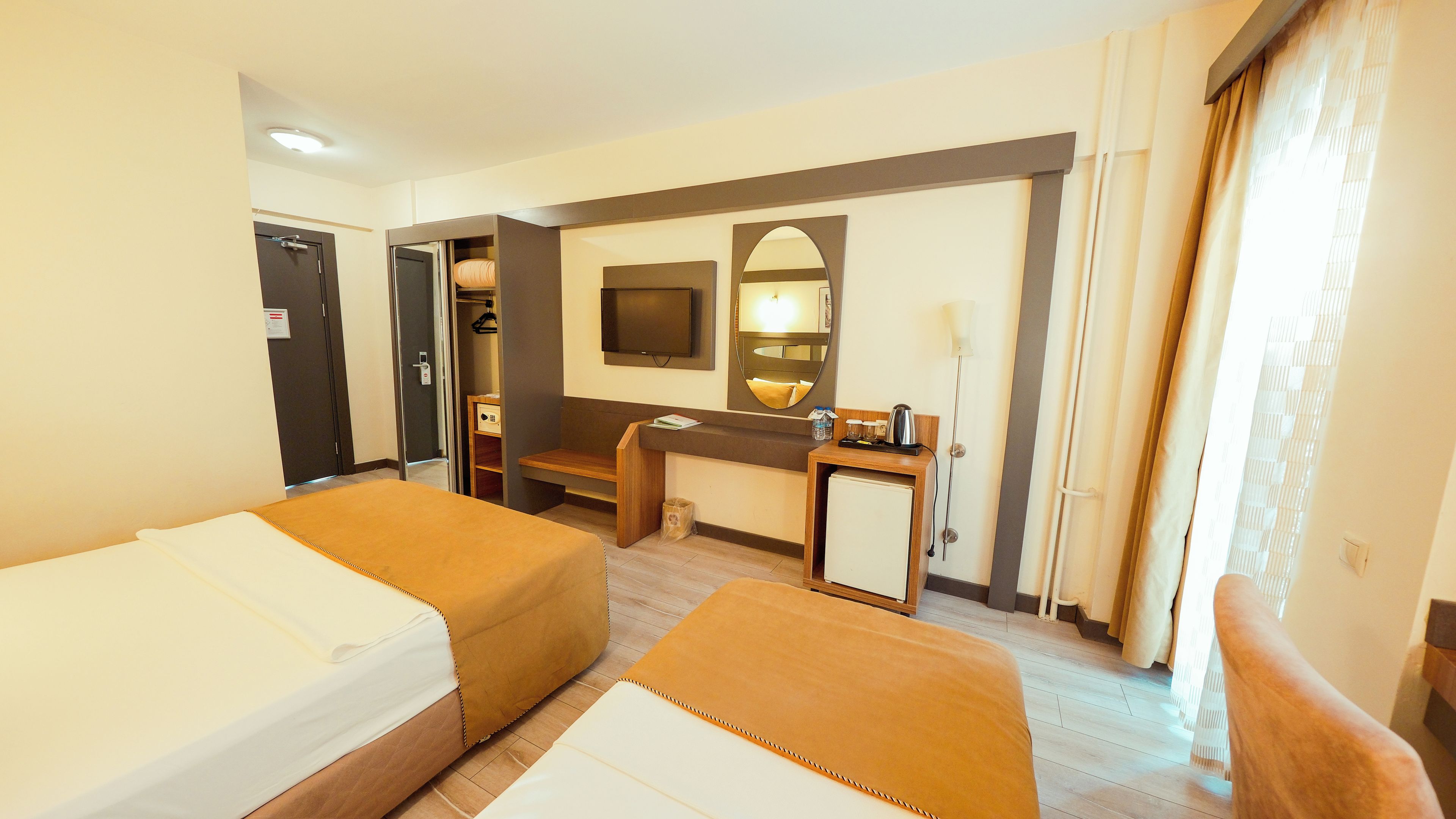 Habitación de hotel con dos camas, un escritorio, un espejo, un televisor y una ventana con cortinas.