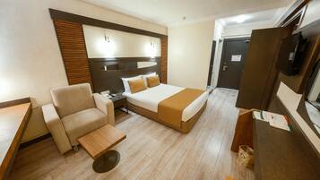 Quarto de hotel com cama, poltrona, mesinha e televisão.