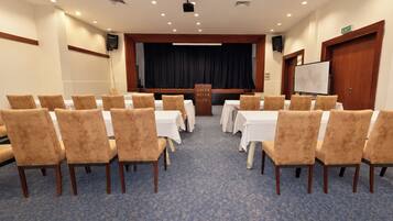 Un salón de conferencias con filas de sillas mirando hacia un escenario, una pizarra y una señal de salida.
