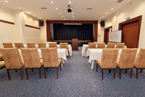 A conference room with rows of chairs facing a stage, a whiteboard, and an exit sign. - Lycus River Thermal Hotel (Denizli)