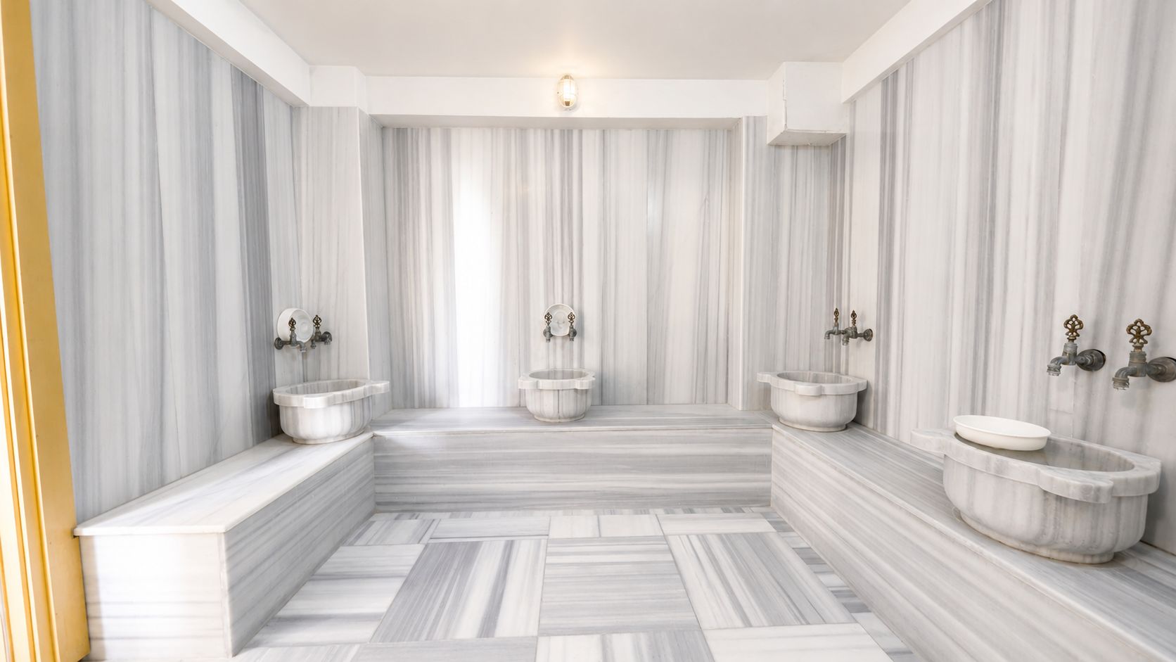 A bathroom with marble walls, multiple sinks, and a central bathtub.