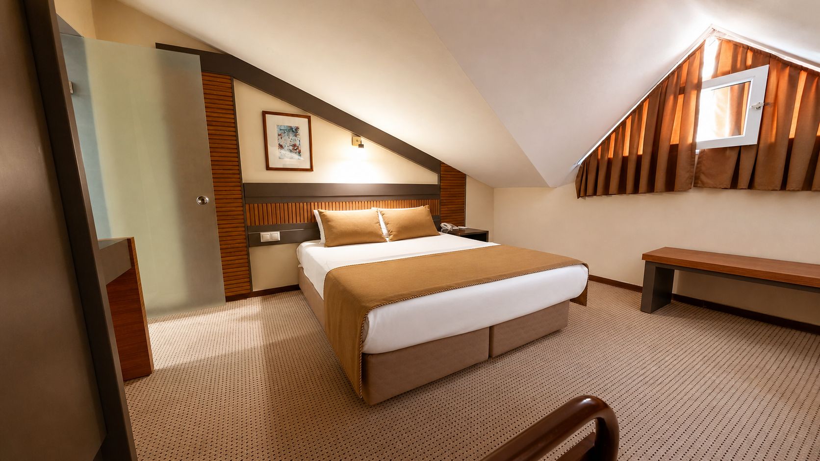 Una habitación de hotel con cama, un banco, un escritorio y una ventana con cortinas.
