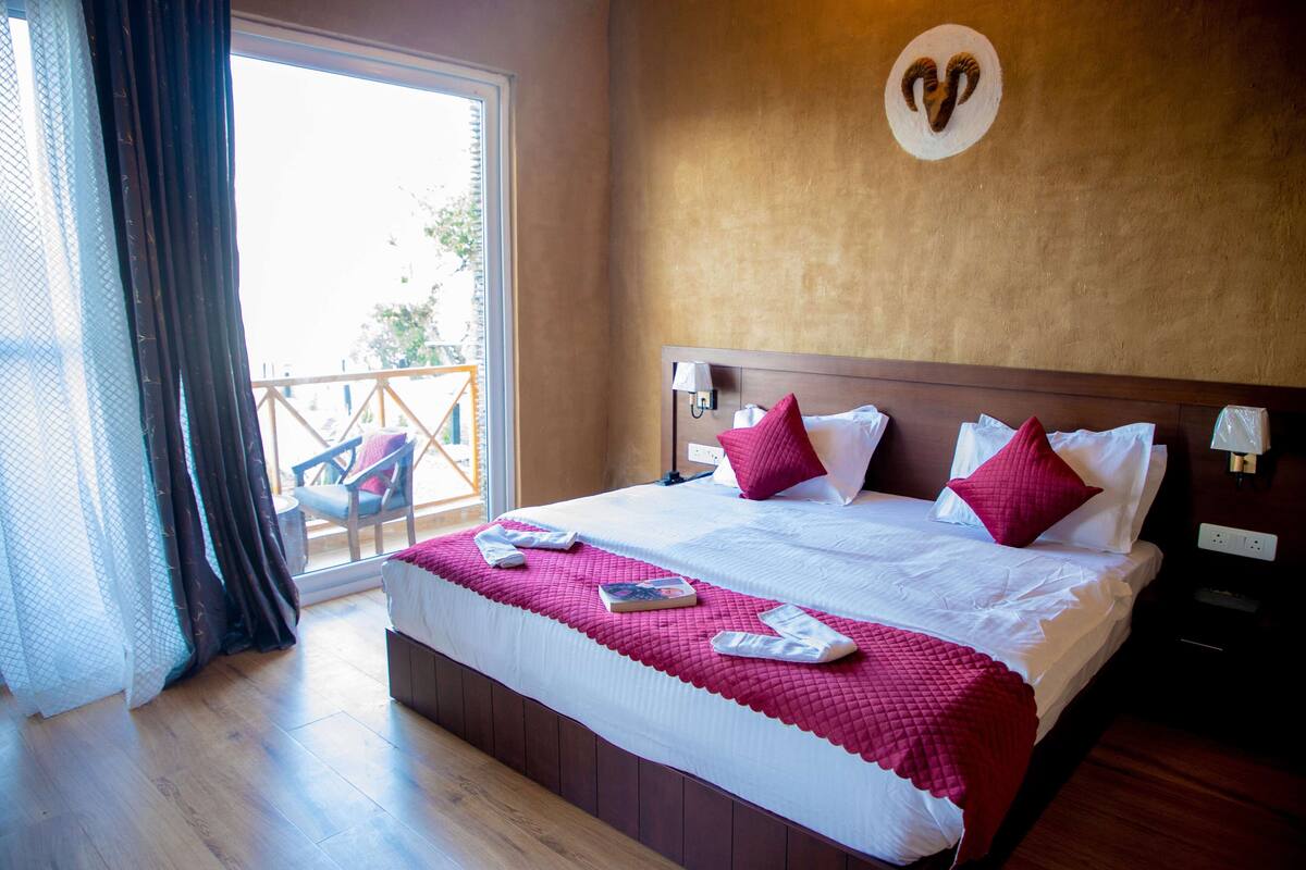 A hotel room with a large bed, a balcony view, and a wooden headboard.