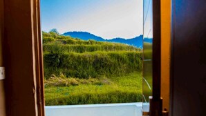 Une porte donnant sur un balcon d’où l’on peut admirer des champs verdoyants et des montagnes lointaines.