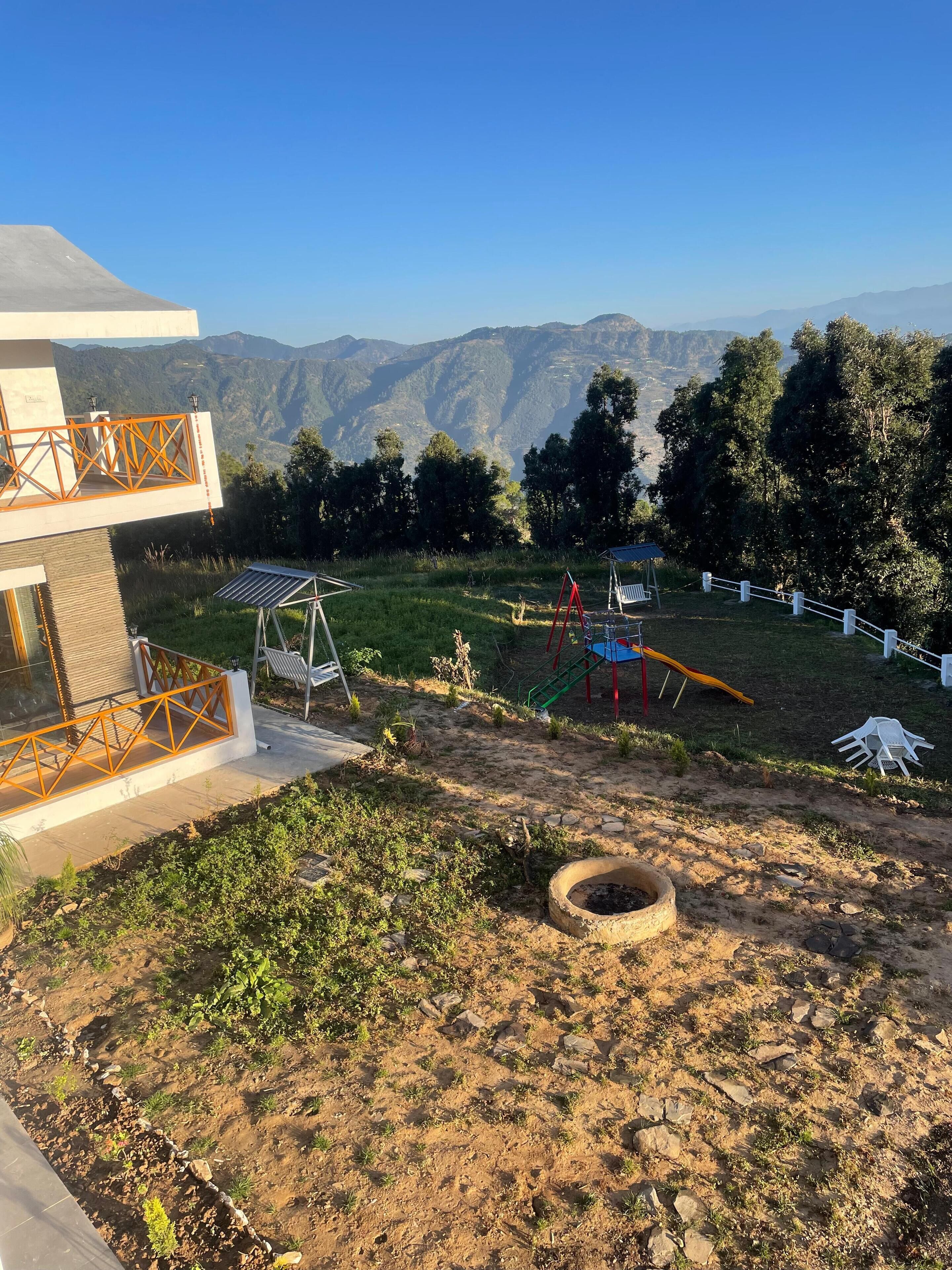 A modern building with a balcony overlooking a playground and a mountainous landscape.