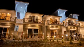 A modern multi-story hotel with balconies, outdoor seating, and a well-lit entrance. - Maatidera Resort-Boutique himalaya stay (Tehri)