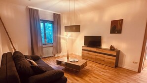 Una sala de estar moderna con un sofá oscuro, una mesa de centro de madera y un televisor sobre un mueble de madera.