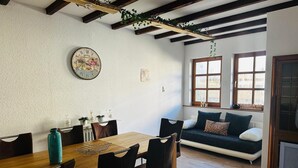 Un comedor con una mesa y sillas de madera, un reloj en la pared y un sofá con cojines.
