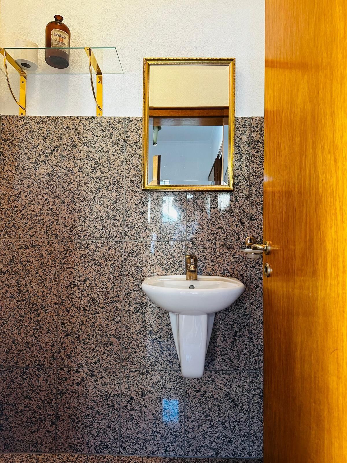 A bathroom with a granite backsplash, a white sink with a gold faucet, and a mirror above the sink.