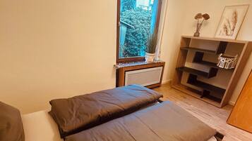 Una camera da letto con un letto, una finestra, un termosifone e una mensola in legno con oggetti decorativi.