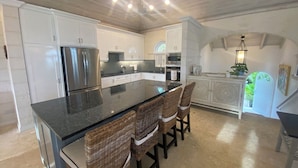 Cozinha moderna com ilha central, eletrodomésticos de aço inoxidável e área de jantar com cadeiras de vime.