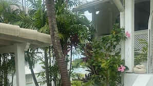 Um edifício branco com área de estar coberta ao ar livre, rodeado por vegetação exuberante e palmeiras.