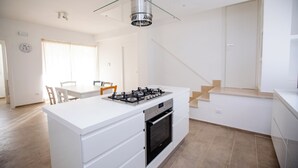 A modern kitchen with a central island, built-in oven, and a glass pendant light. - Homidoo BellaVita Apartment (Pachino)