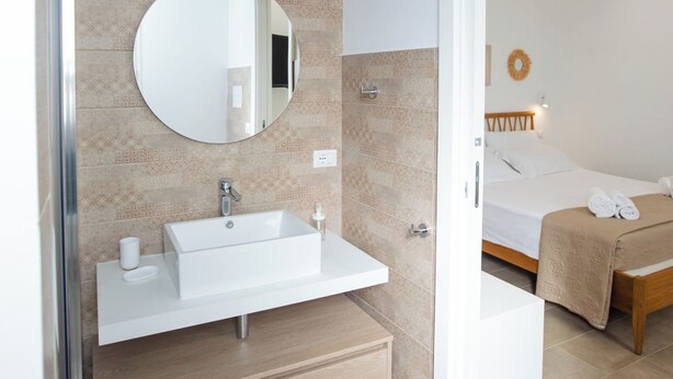 A modern bathroom with a white sink, mirror, and beige tiles. - Homidoo BellaVita Apartment (Pachino)
