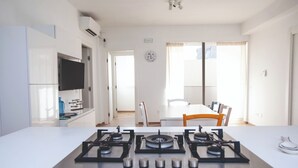 A modern kitchen with a gas stove, a flat-screen TV mounted above the counter, and a dining area with a table and chairs. - Homidoo BellaVita Apartment (Pachino)