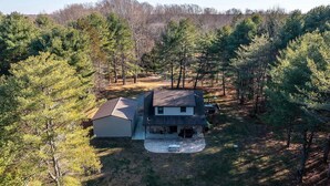 A two-story house with a garage, surrounded by a wooded area.